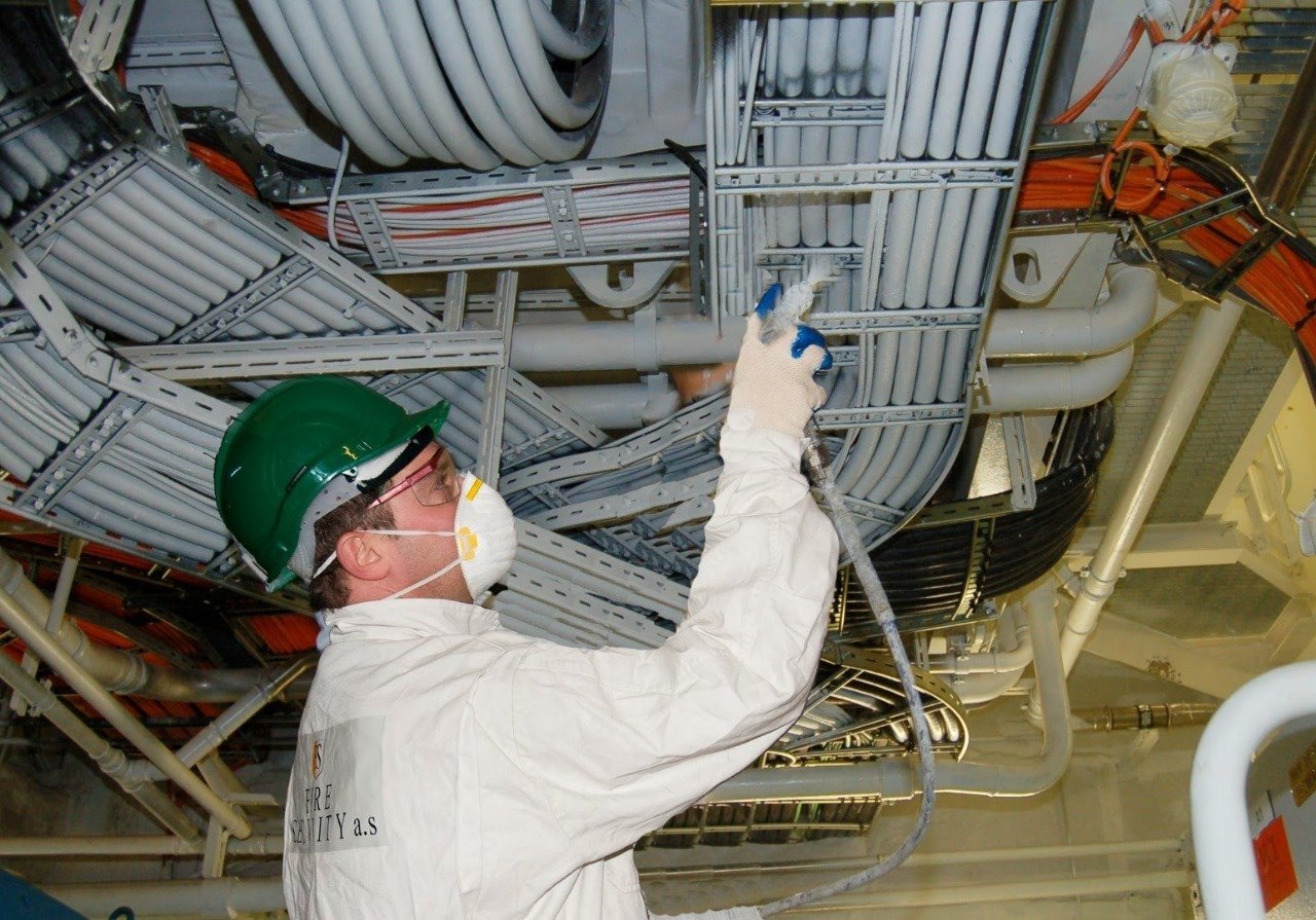 Fire protection specialist applying cable coating to electrical cable trays in an industrial facility in Saudi Arabia